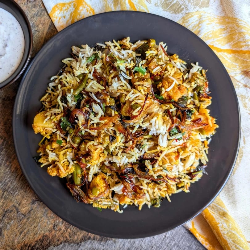 A plate of Shawarma House's chicken biryani with rice, vegetables, and fried onions, served with a side of sauce.
