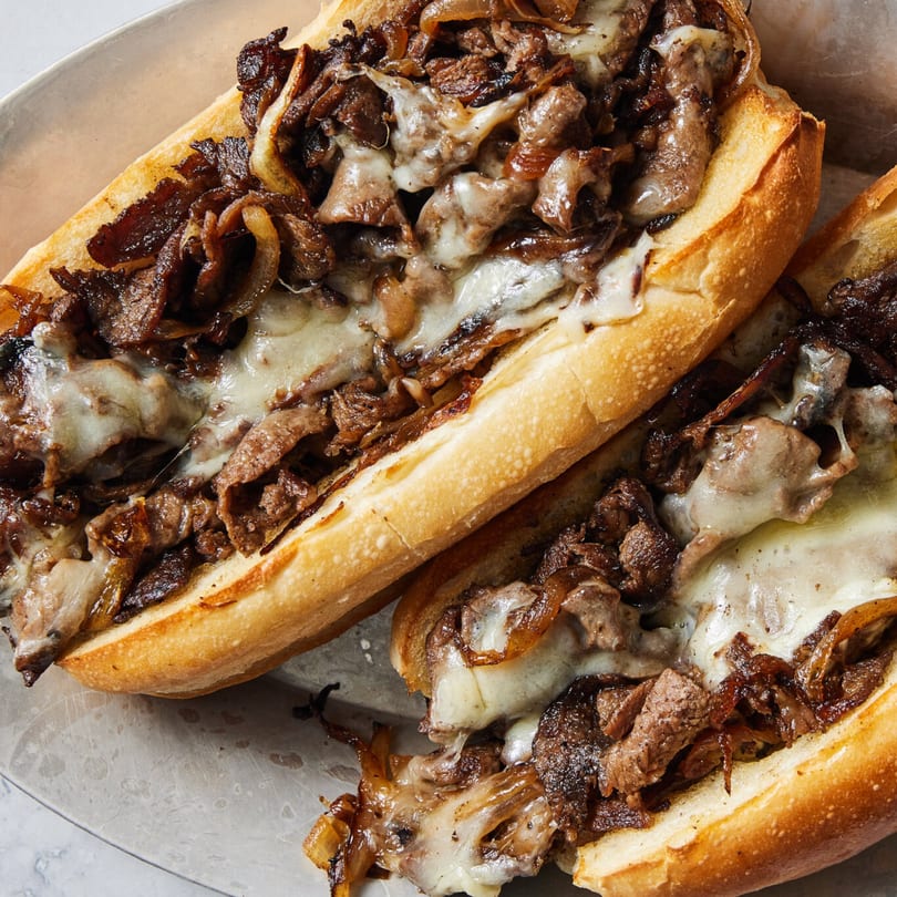 Two Shawarma House cheesesteak sandwiches, filled with steak, caramelized onions, and melted cheese.